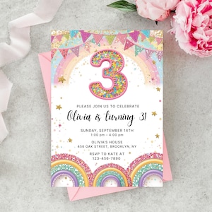 May include: A birthday invitation in a pink envelope. The invitation features a colourful design with a large number 3, rainbows, stars, and text that reads "Olivia is turning 3!" and event details.