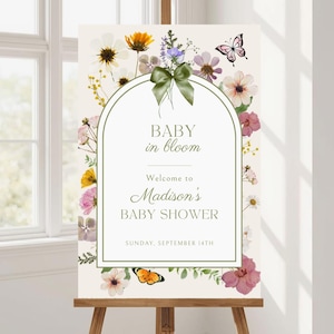 Puede incluir: Un letrero de bienvenida para baby shower con el texto "BABY in bloom" y "Welcome to Madison's BABY SHOWER". El letrero está adornado con ilustraciones florales y de mariposas y un lazo verde. La fecha es domingo 14 de septiembre.
