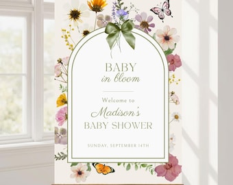 May include: A baby shower welcome sign with the text "BABY in bloom" and "Welcome to Madison's BABY SHOWER". The sign is decorated with floral and butterfly illustrations and a green bow. The date is Sunday, September 14th.