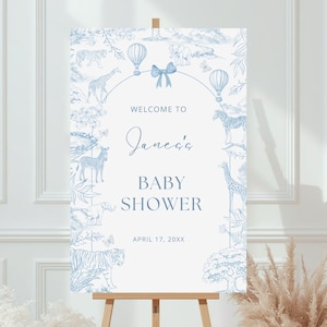 Op de afbeelding: Een welkomstbord voor een babyshower op een ezel. Het witte bord toont blauwe illustraties van dieren, luchtballonnen en bladeren. De tekst luidt "Welkom bij Jane's Baby Shower" en de datum.