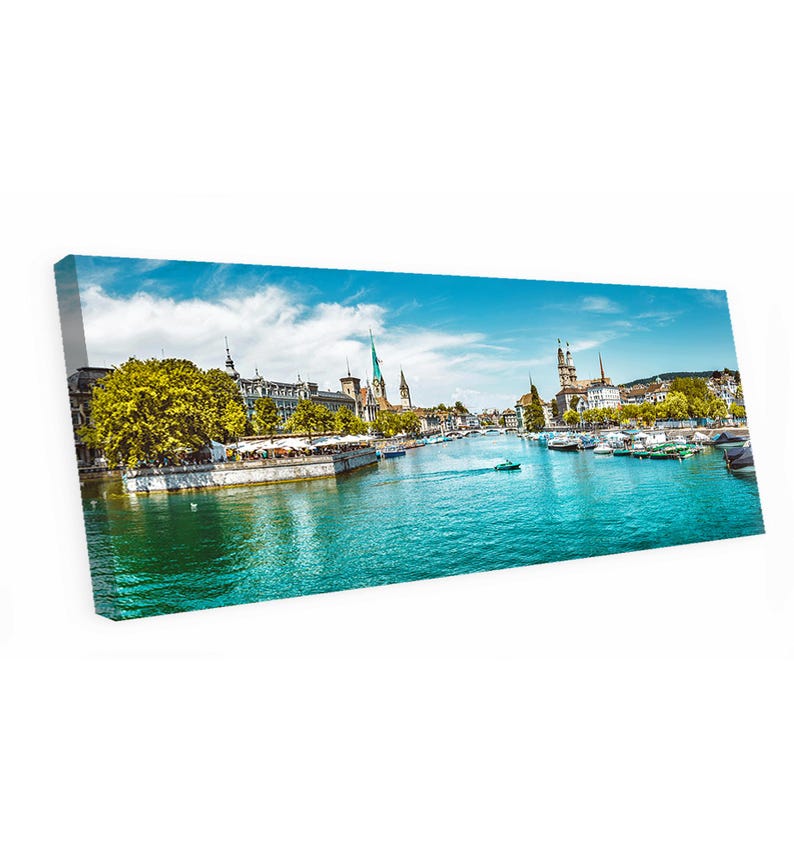 May include: A canvas print of a scenic European cityscape. The image features a river with boats, buildings with spires, and a bright blue sky with clouds. The water is a vibrant turquoise color.