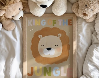 May include: A framed art print featuring a cartoon lion with a brown mane and closed eyes. The text "KING OF THE JUNGLE" is displayed in colorful letters above and below the lion illustration. The artwork is set against a beige background.