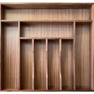 May include: A wooden cutlery tray with multiple compartments. The tray is made of a light brown wood with a visible grain pattern. It features various sized rectangular compartments for organizing silverware and utensils.