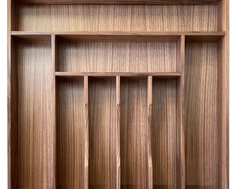 Puede incluir: Una bandeja de cubiertos de madera con múltiples compartimentos. La bandeja está hecha de madera de color marrón claro con un patrón de vetas visible. Cuenta con compartimentos rectangulares de varios tamaños para organizar la cubertería y los utensilios.