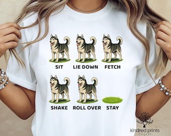 May include: White t-shirt featuring a graphic of a husky dog demonstrating commands: sit, lie down, fetch, shake, roll over, and stay. The text is in black, with the dog illustrations in gray and white. The shirt has a crew neck.