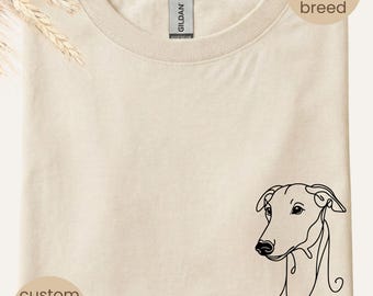 May include: Beige t-shirt with a line drawing of a dog's head and the name "Ted" in black. The shirt has a crew neck and is folded. Text on the shirt says "your dog's breed" and "custom dog name".