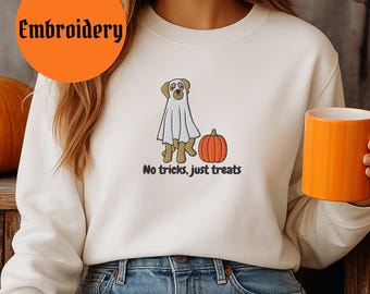 Puede incluir: Sudadera de color crema con un gráfico de perro con temática de Halloween. El diseño presenta un perro con un disfraz de fantasma junto a una calabaza naranja, con el texto "No tricks, just treats" debajo. La palabra "Embroidery" está en un círculo naranja.