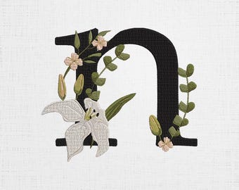 May include: Black embroidered letter N with white flowers and green leaves.