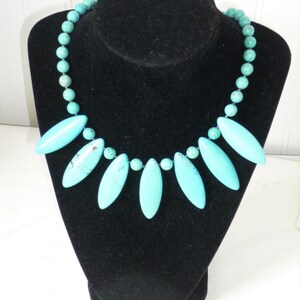 May include: A turquoise necklace with a row of round beads and a pendant of seven teardrop-shaped turquoise stones.