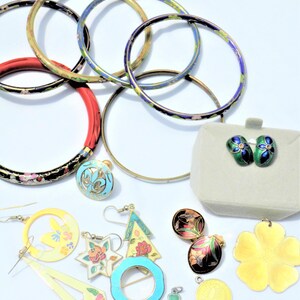 May include: A collection of cloisonné jewelry featuring a variety of colors and designs, including flowers, stars, and geometric shapes. The jewelry includes earrings, a brooch, a ring, and several bracelets.