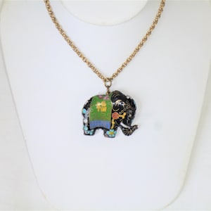 May include: A gold chain necklace with a black enamel elephant pendant. The elephant is decorated with green, blue, and white enamel and has a gold Chinese character on its side.