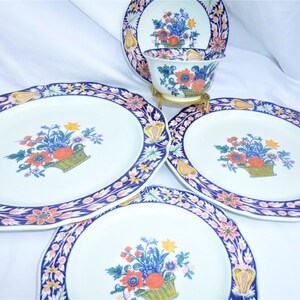 May include: Set of four white ceramic plates with blue, pink, and yellow floral designs. The plates feature a scalloped edge and a floral motif with a basket of flowers.