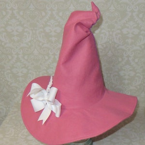 Puede incluir: Un sombrero de bruja de fieltro rosa con un ala ancha y un lazo de sat&eacute;n blanco.