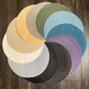 May include: A set of 10 round placemats in various colors and textures, including beige, gray, black, blue, and purple. The placemats are arranged in a circular pattern, with the darkest colors in the center and the lighter colors on the outside.