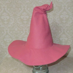 Puede incluir: Un sombrero de bruja de fieltro rosa con una corona alta y puntiaguda y un ala ancha.