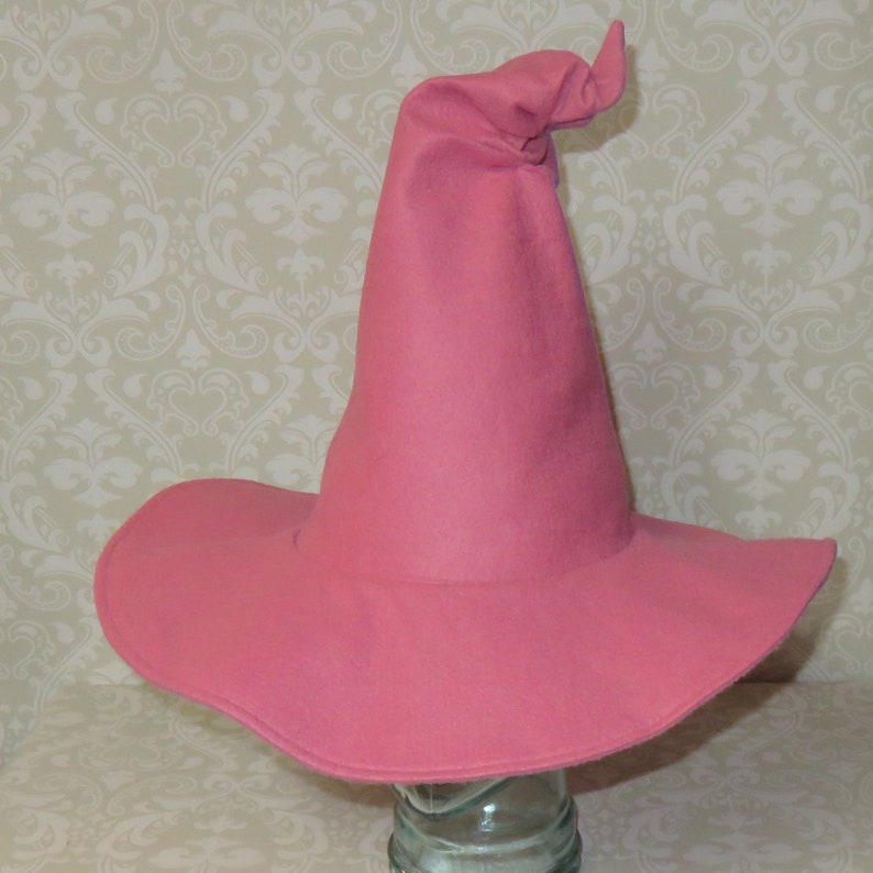 Puede incluir: Un sombrero de bruja de fieltro rosa con una corona alta y puntiaguda y un ala ancha.