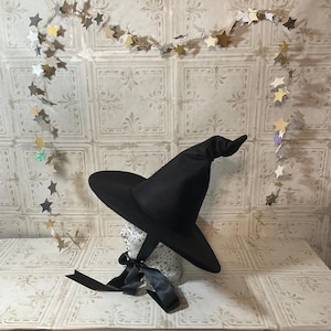 May include: A black witch hat with a wide brim and a tall pointed crown. The hat is made of felt and has a satin ribbon tied around the base.