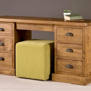 May include: A wooden desk with multiple drawers and a matching stool. The desk has a natural wood finish and black metal handles. A small potted plant and a book rest on the desk's surface. The stool is upholstered in a light green fabric.