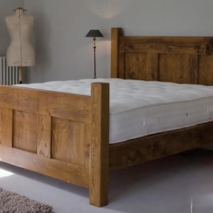 May include: A wooden bed frame with a white mattress. The bed frame is made of light brown wood and has a headboard and footboard. The room has a neutral colour scheme with a rug and a lamp.