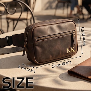 May include: A brown leather fanny pack with a front zipper pocket and the gold-colored initials NK. The bag features a black adjustable strap with a plastic buckle. Dimensions are 8.6 inches wide, 5.5 inches high, and 2.3 inches deep.