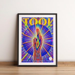 Könnte beinhalten: Ein gerahmtes Konzertplakat der Band TOOL mit einer lebendigen, psychedelischen Illustration einer Hand mit einem Auge in der Handfläche vor einem blau-gelben Strahlenhintergrund. Der Text lautet TOOL, March 20th, 2022, Rocket Mortgage Fieldhouse.