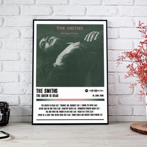 May include: A framed poster featuring the album art for The Smiths' "The Queen Is Dead." The image is a black and white photo of a person. The poster includes the band's name, album title, and tracklist.