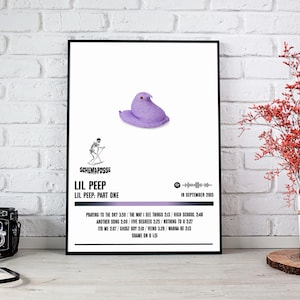 May include: A framed poster featuring a purple marshmallow peep on a white background. The poster includes the text "Lil Peep: Part One" and a list of song titles. A black frame surrounds the poster. The poster is displayed on a white brick wall.