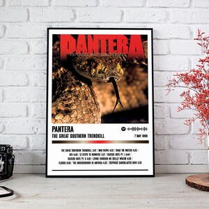 May include: Black framed poster featuring the band name "PANTERA" in red, with a close-up of a snake's head. The poster includes the album title "THE GREAT SOUTHERN TRENDKILL" and a tracklist. A vintage camera and a vase with red flowers are in the foreground.