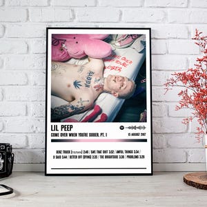 May include: A black and white poster with a photo of Lil Peep, a musician, lying on a bed with a pink stuffed animal. The poster has the title "Come Over When You're Sober, Pt. 1" and the date "15 August 2017". The poster also lists the track titles and lengths from the album.