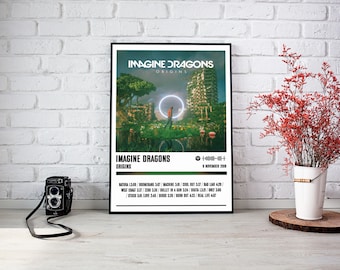 Puede incluir: Un póster enmarcado con la portada del álbum "Origins" de Imagine Dragons. La obra de arte muestra un paisaje surrealista con un anillo brillante y texto. Una cámara vintage está frente al póster. Flores rojas en un cubo blanco a la derecha.
