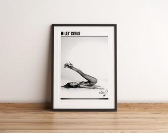 Könnte beinhalten: Schwarzweiß-Fotodruck von Miley Cyrus in einem schwarzweißen Outfit, die auf dem Rücken liegt und die Beine in die Luft streckt. Der Druck ist in einem schwarzen Rahmen gerahmt und trägt oben den Text "MILEY CYRUS".