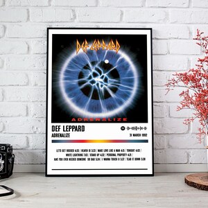 May include: A white poster with a black border featuring a Def Leppard album cover. The album cover is a close-up of a blue eye with a white pupil and a white circle in the center. The album title "Adrenalize" is printed in red and black letters. The album release date "31 March 1992" is printed in black letters. The album track list is printed in black letters below the album title.