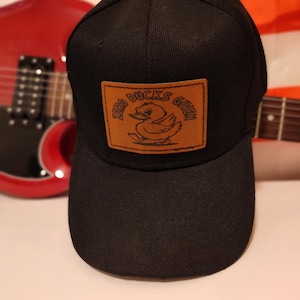 May include: Black baseball cap with a brown leather patch that says "Zero Ducks Given" with a cartoon duck illustration.