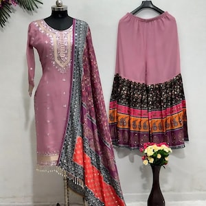 May include: A mauve-coloured, long-sleeved tunic with detailed embroidery and embellishments, alongside matching palazzo trousers and a patterned scarf. The scarf has a vibrant mix of colours and decorative trim. A complete ensemble.