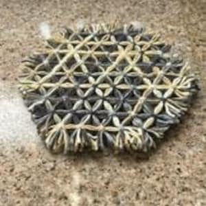 May include: A woven coaster with a geometric pattern in shades of gray and beige.