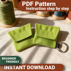 May include: Two small, square, lime green fabric pouches with fold-over flaps and stitched rectangular details. One pouch features a black fabric loop attached to a silver metal keyring. The image includes text reading PDF Pattern, Instruction step by step, BEGINNER FRIENDLY, and INSTANT DOWNLOAD.