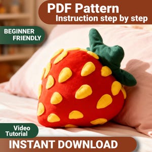 Pode incluir: Uma almofada vermelha em forma de morango com detalhes de sementes amarelas e um caule verde. A imagem inclui o texto que diz "PDF Pattern", "Beginner Friendly", "Video Tutorial" e "Instant Download".