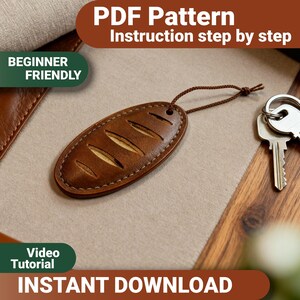 May include: An oval-shaped brown leather keychain featuring a bread-like design with three diagonal cutouts, stitched edges, and a thin brown cord. The image includes text stating PDF Pattern, Instruction step by step, BEGINNER FRIENDLY, Video Tutorial, and INSTANT DOWNLOAD.
