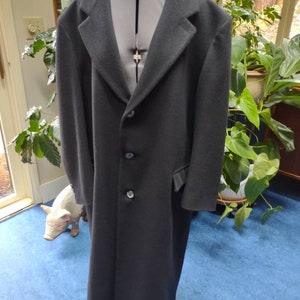 May include: A long black wool coat with a single breasted closure and four buttons. The coat has a classic style and a tailored fit.