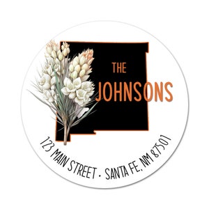 May include: A round sticker with a black and orange outline of the state of New Mexico. The sticker features a white floral design and the text "The Johnsons" in orange. The address "123 Main Street, Santa Fe, NM 87501" is printed in black at the bottom.