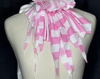 Puede incluir: Un collar de tela a rayas rosa y blancas con bordes deshilachados. El collar está plisado y tiene un diseño con volantes.