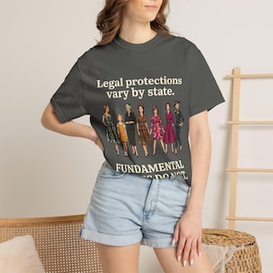 Puede incluir: Una camiseta de manga corta gris carbón con un gráfico de siete mujeres con ropa de estilo vintage. El texto dice Legal protections vary by state. FUNDAMENTAL RIGHTS DO NOT. La camiseta se combina con pantalones cortos de mezclilla azul claro.