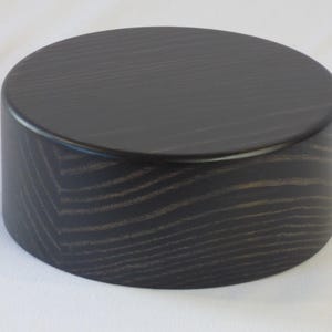 May include: A black wooden round pedestal with a smooth, polished surface and visible wood grain.