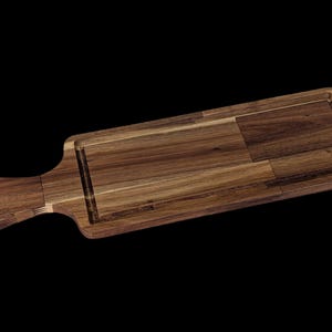 Op de afbeelding: Een rechthoekig houten serveerplank met een handvat en een verzonken gedeelte. De plank is gemaakt van donkerbruin hout met een natuurlijk nerfpatroon. Het handvat heeft een gat om op te hangen. De plank is ongeveer 40 cm lang.