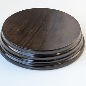 Può includere: Un espositore rotondo in legno marrone scuro con una parte superiore rotonda e tre anelli rialzati attorno alla base.