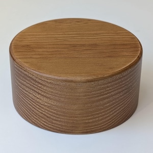 Peut inclure: Un présentoir rond en bois avec une finition brun clair. Le présentoir a une surface supérieure lisse et un motif texturé en grain de bois sur les côtés.
