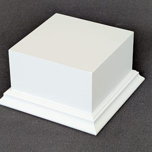 Peut inclure: Un présentoir carré blanc avec une base décorative. Le présentoir est fait d'un matériau solide et est peint en blanc. La base a un design détaillé et superposé. Le présentoir est conçu pour mettre en valeur des objets.
