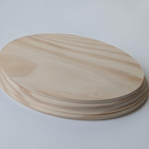 Könnte beinhalten: Ein ovaler Rohling aus Naturholz für Bastelarbeiten. Das Holz ist hellbraun und hat eine glatte Oberfläche. Der Rohling besteht aus mehreren Holzschichten.