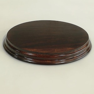Könnte beinhalten: Ein runder, dunkelbrauner Holzständer mit glatter, polierter Oberfläche. Der Ständer hat einen erhöhten Rand und eine leicht abgerundete Lippe.