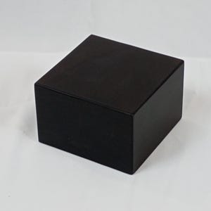 Peut inclure: Une boîte carrée en bois noire avec une surface lisse.